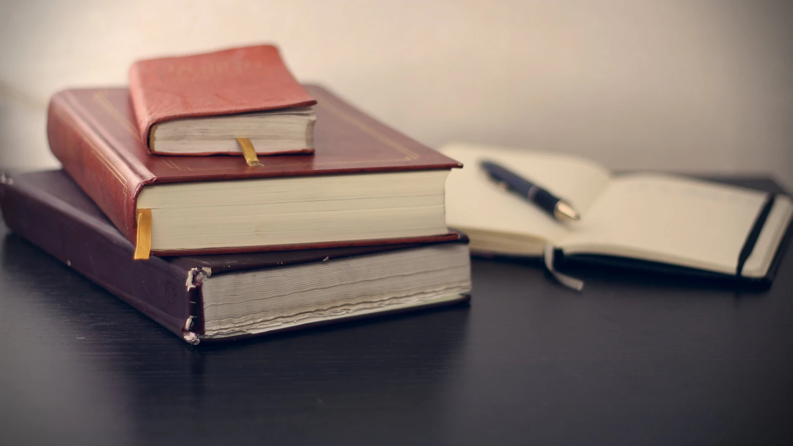 A stack of leather-bound law books beside an open notebook and a pen on a dark desk
