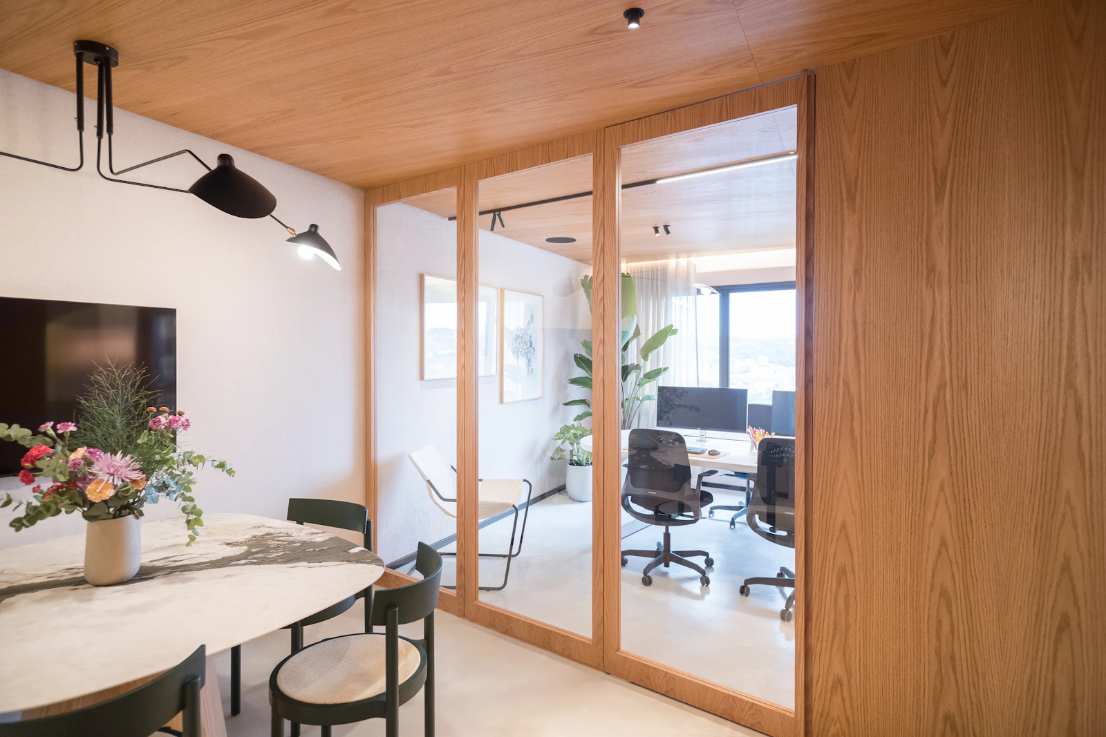 Our office, with a glass and timber partition, a meeting table with fresh flowers and a desk by the window beyond