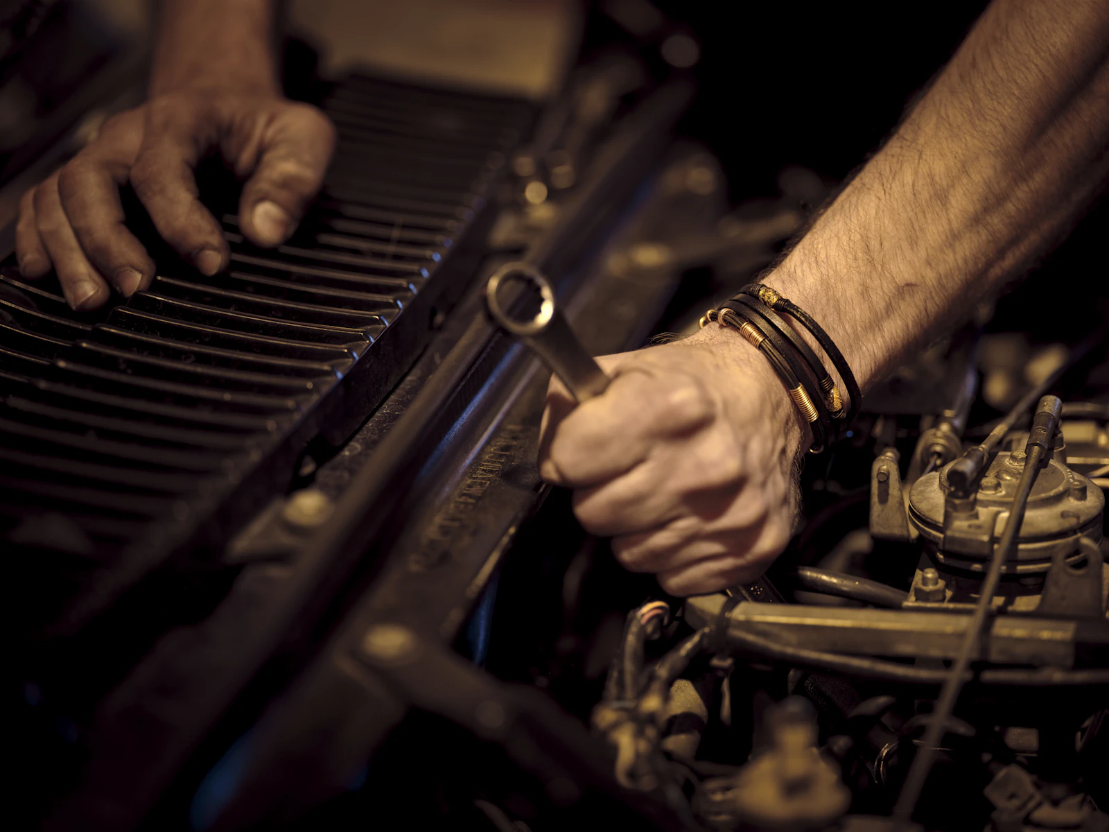 A mechanic’s hands holding a spanner over an open engine bay